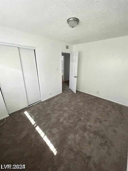 unfurnished bedroom with a textured ceiling, a closet, and dark colored carpet