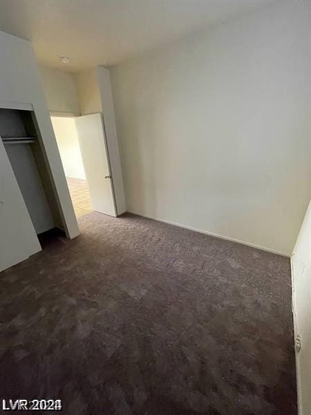 unfurnished bedroom with dark colored carpet and a closet