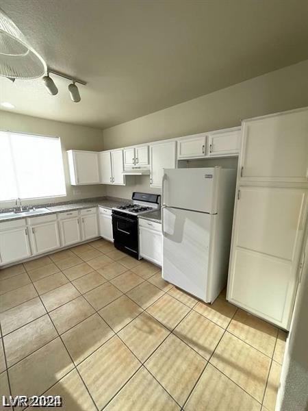 kitchen with white cabinets, range with gas stovetop, white refrigerator, sink, and rail lighting