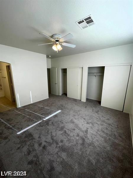 unfurnished bedroom with ceiling fan, two closets, and dark colored carpet