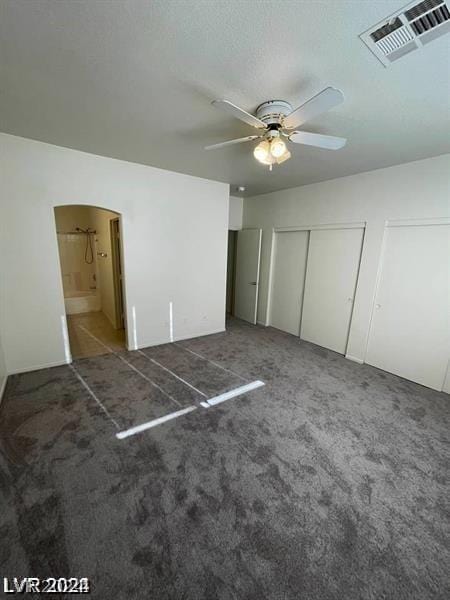 unfurnished bedroom featuring ceiling fan, dark carpet, a closet, and ensuite bath