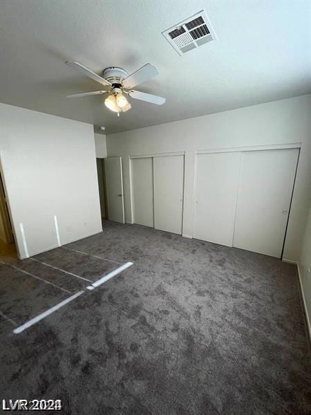 unfurnished bedroom featuring ceiling fan, dark colored carpet, and multiple closets