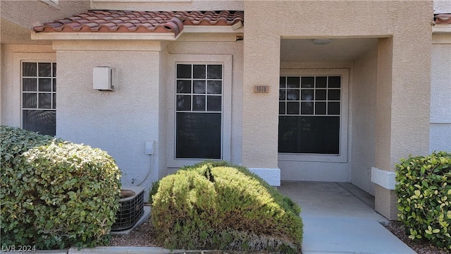 entrance to property with cooling unit, a patio area, a tiled roof, and stucco siding