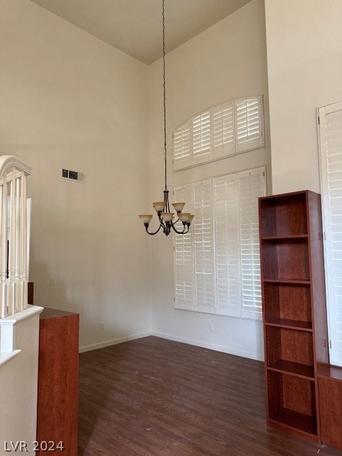 unfurnished dining area with dark hardwood / wood-style flooring, an inviting chandelier, and a high ceiling