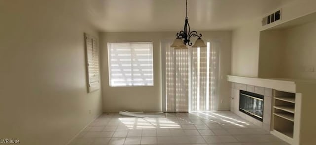 unfurnished living room featuring a chandelier, light tile patterned floors, built in shelves, and a tile fireplace