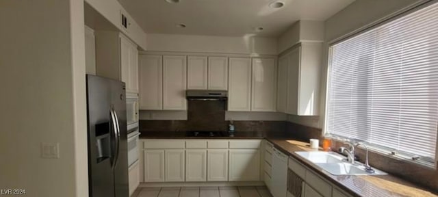 kitchen with light tile patterned flooring, sink, white dishwasher, stainless steel refrigerator with ice dispenser, and white cabinets