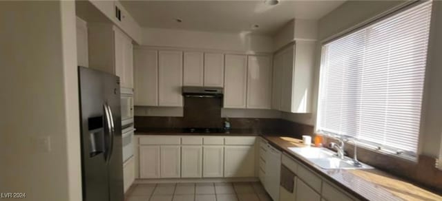 kitchen featuring a healthy amount of sunlight, white cabinets, light tile patterned floors, sink, and white appliances