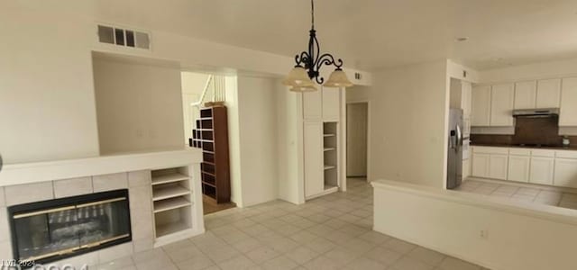 interior space featuring light tile patterned flooring, a tile fireplace, tile counters, hanging light fixtures, and white cabinets