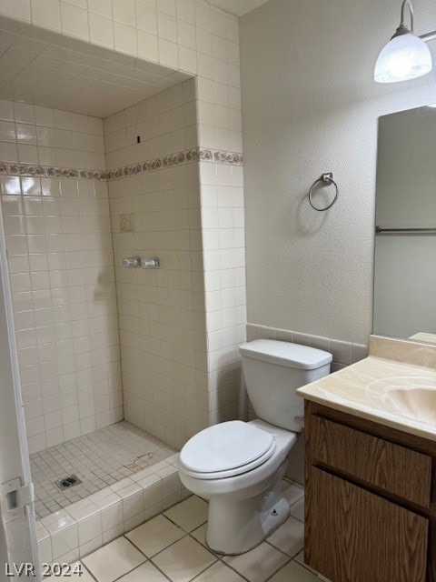 bathroom featuring tile patterned flooring, toilet, vanity, and a tile shower