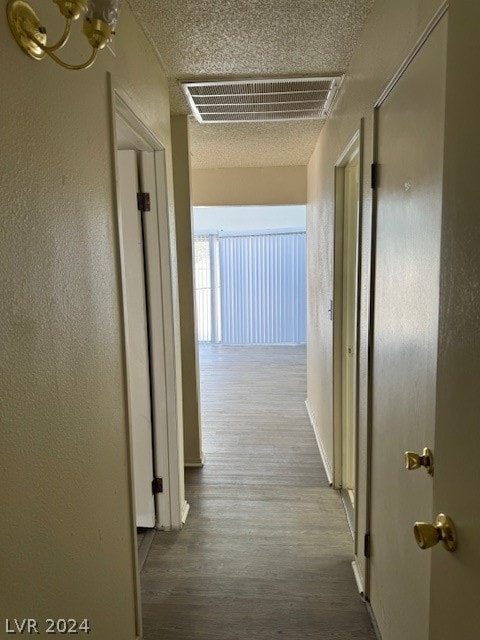 hall with a textured ceiling, a notable chandelier, and wood-type flooring