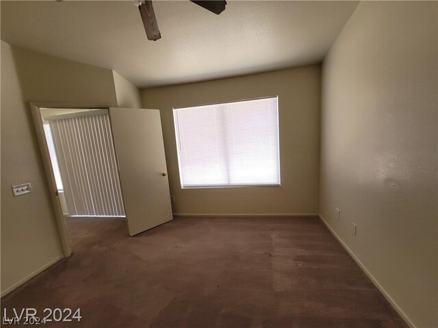 unfurnished room with ceiling fan and dark carpet