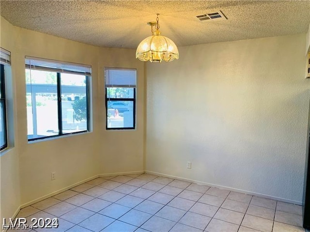 unfurnished room featuring a textured ceiling, light tile patterned floors, and a notable chandelier