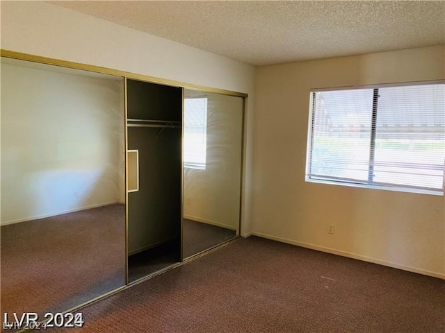 unfurnished bedroom with dark carpet, a closet, and a textured ceiling