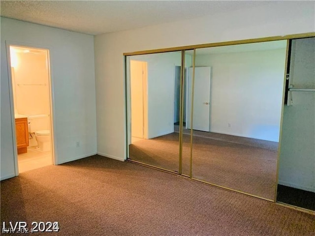 unfurnished bedroom with a closet, ensuite bathroom, and carpet flooring