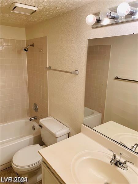 full bathroom featuring vanity, toilet, tiled shower / bath, and a textured ceiling