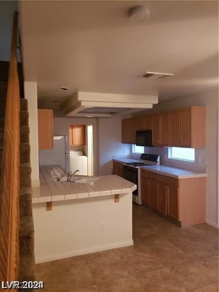 kitchen with tile counters, washer / clothes dryer, kitchen peninsula, and white gas range oven