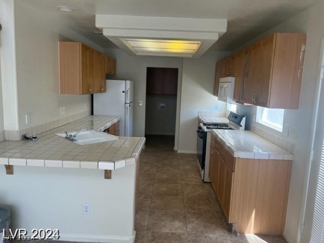 kitchen with white appliances, dark tile patterned floors, kitchen peninsula, tile countertops, and a breakfast bar