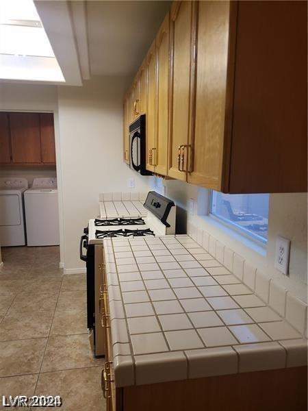 kitchen featuring light tile patterned floors, tile countertops, gas range oven, and washer and dryer