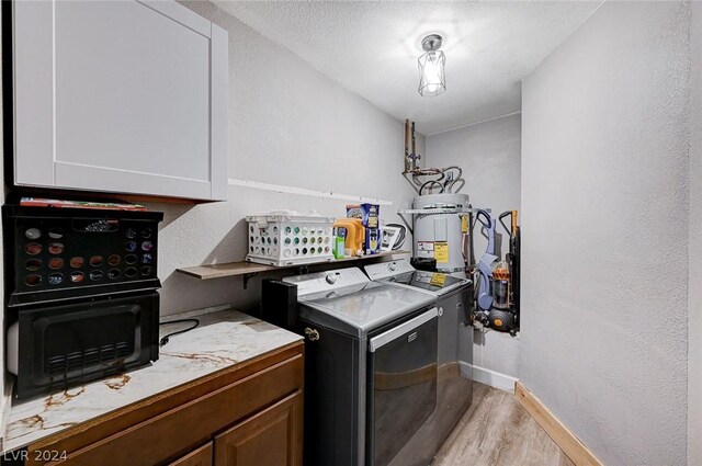 laundry area featuring cabinets, a textured ceiling, water heater, washing machine and clothes dryer, and light hardwood / wood-style floors