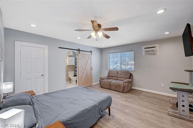 bedroom with connected bathroom, ceiling fan, a barn door, an AC wall unit, and light wood-type flooring