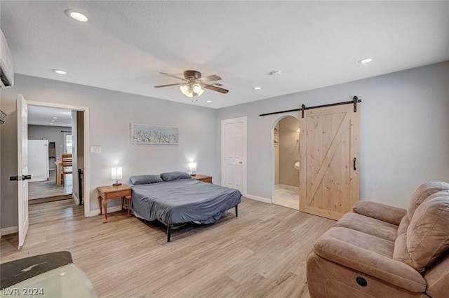 bedroom featuring ceiling fan, a barn door, and light wood-type flooring