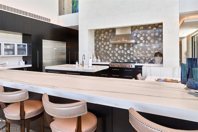 kitchen featuring stainless steel appliances, wall chimney range hood, backsplash, and a breakfast bar area