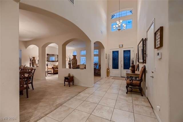 foyer entrance featuring light tile patterned flooring, light colored carpet, a high ceiling, french doors, and an inviting chandelier