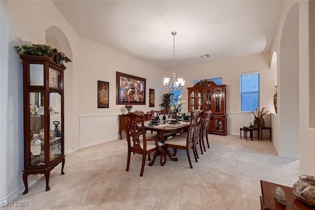 dining area with light carpet, arched walkways, a chandelier, and wainscoting