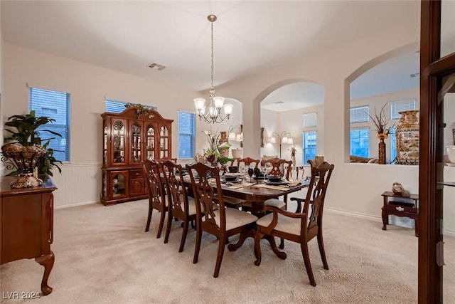 dining space with light carpet, a wainscoted wall, a chandelier, and visible vents