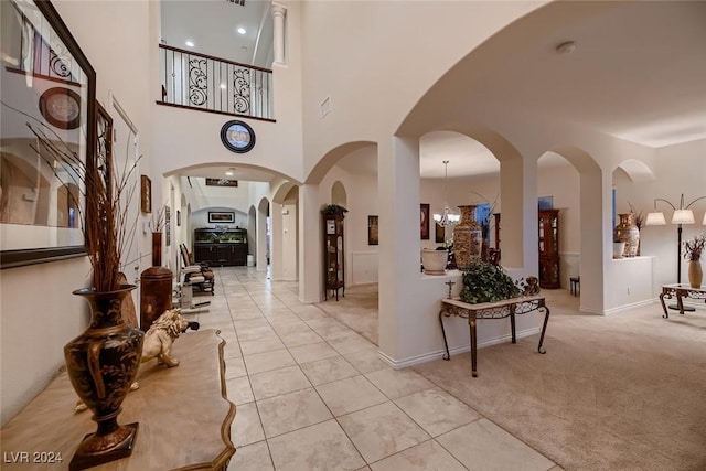 hall featuring arched walkways, visible vents, light colored carpet, a towering ceiling, and light tile patterned flooring