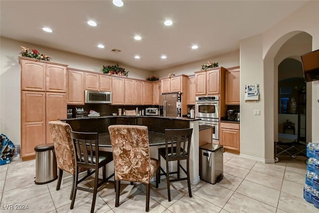 kitchen featuring arched walkways, stainless steel appliances, a breakfast bar, and dark countertops