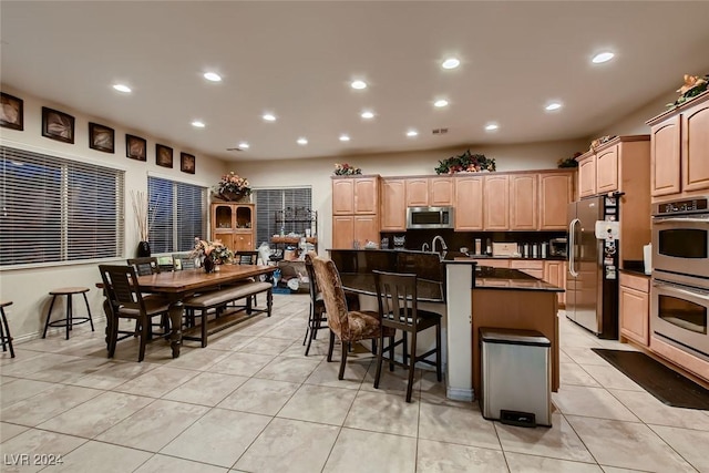 kitchen featuring light tile patterned flooring, a breakfast bar, appliances with stainless steel finishes, an island with sink, and dark countertops