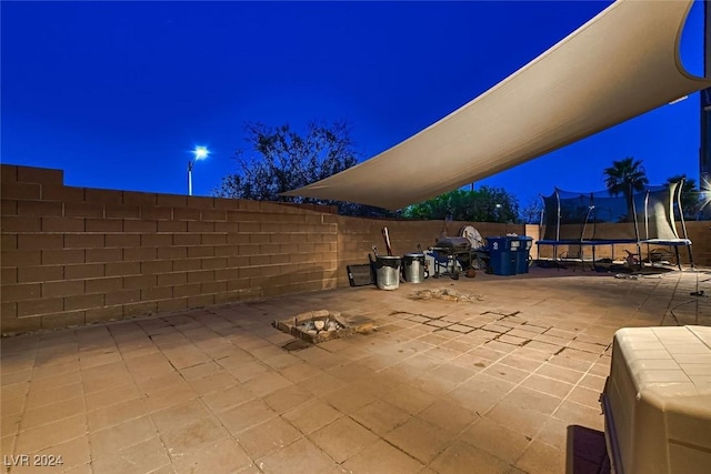 patio at twilight featuring a trampoline and fence