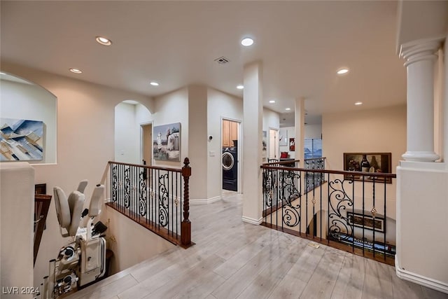 hallway featuring wood finished floors, visible vents, an upstairs landing, washer / clothes dryer, and ornate columns