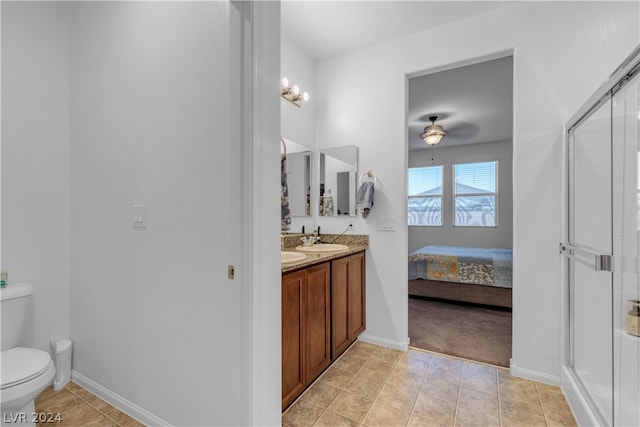 ensuite bathroom featuring double vanity, toilet, a sink, a shower stall, and baseboards