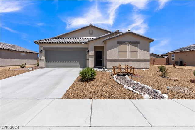 view of front facade with central AC unit, concrete driveway, a tile roof, an attached garage, and stucco siding