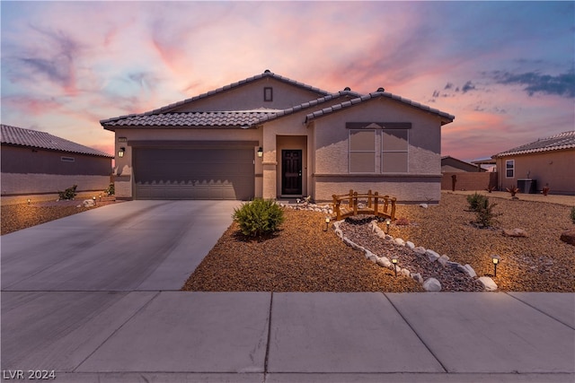 mediterranean / spanish-style house featuring a garage, central AC, a tile roof, concrete driveway, and stucco siding