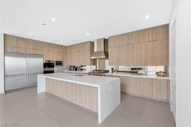 kitchen with appliances with stainless steel finishes, light tile patterned floors, sink, and wall chimney range hood