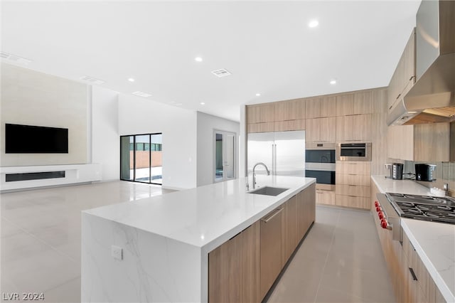 kitchen with a kitchen island with sink, stainless steel appliances, sink, wall chimney exhaust hood, and light brown cabinets