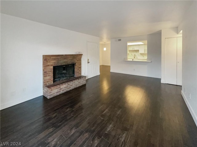 unfurnished living room featuring dark wood-type flooring and a brick fireplace