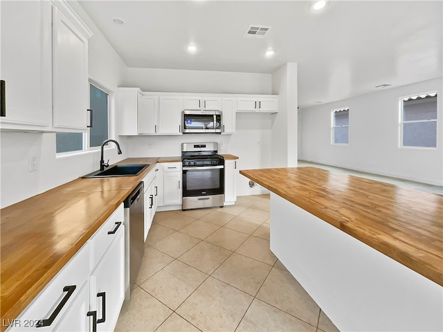 kitchen featuring sink, light tile patterned flooring, butcher block counters, white cabinetry, and stainless steel appliances