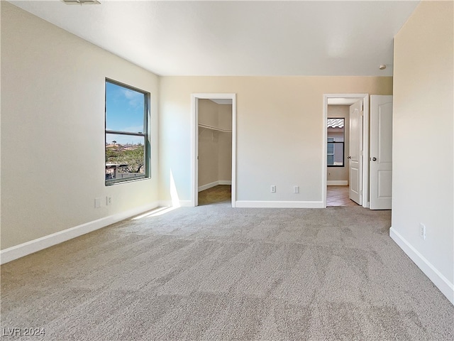 unfurnished bedroom with light carpet, a walk in closet, and a closet