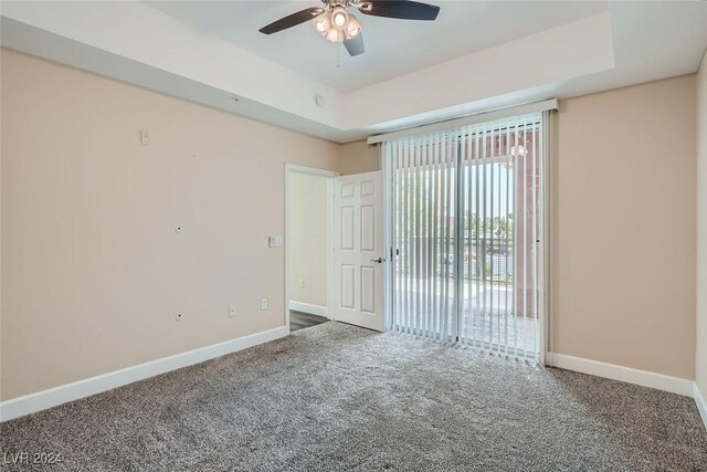 unfurnished room featuring a raised ceiling, carpet, and ceiling fan