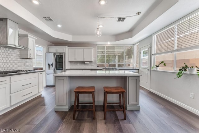 kitchen with white cabinets, appliances with stainless steel finishes, wall chimney exhaust hood, a kitchen island, and a raised ceiling