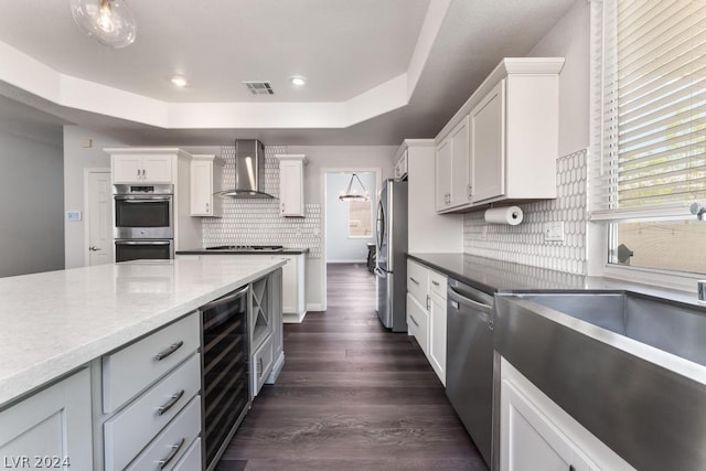 kitchen with appliances with stainless steel finishes, white cabinetry, wine cooler, and wall chimney range hood