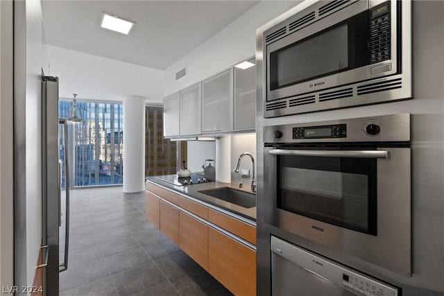 kitchen with appliances with stainless steel finishes, white cabinets, floor to ceiling windows, dark tile patterned floors, and sink