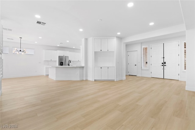 unfurnished living room featuring an inviting chandelier, light hardwood / wood-style flooring, and sink