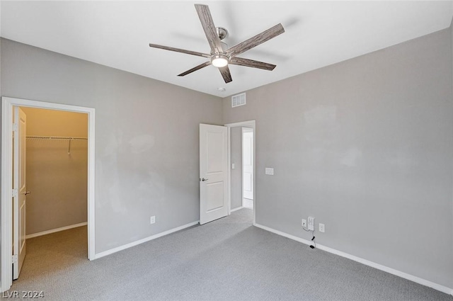 unfurnished bedroom with ceiling fan, a closet, a spacious closet, and carpet