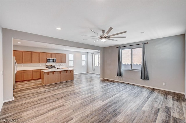 kitchen featuring appliances with stainless steel finishes, an island with sink, sink, ceiling fan, and light wood-type flooring