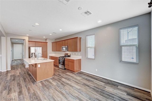 kitchen with sink, appliances with stainless steel finishes, hardwood / wood-style floors, a kitchen breakfast bar, and an island with sink